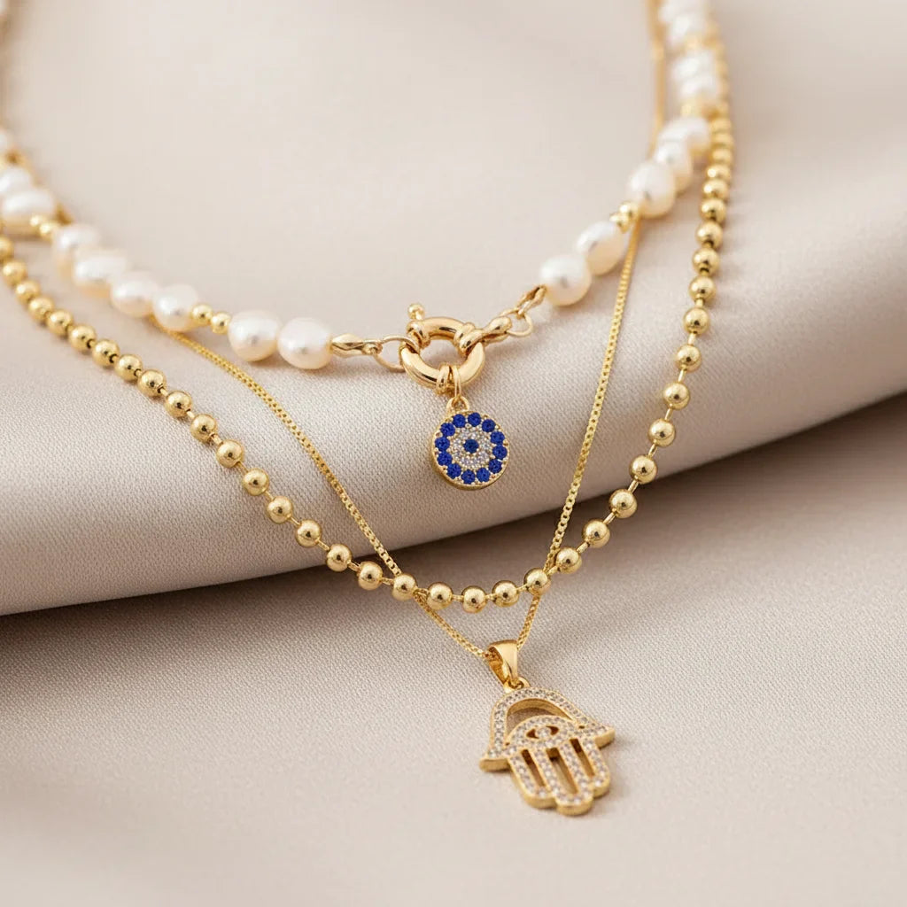 Composition de colliers multi-rangs style bohème chic : choker perles d'eau douce avec pendentif mauvais œil bleu, chaîne à billes dorée et collier main de Fatma strass.