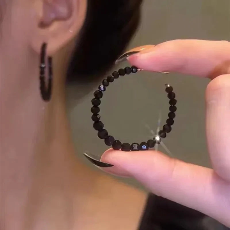 Boucles d'oreilles créoles ouvertes composées de perles à facettes noires, monture dorée - Style chic et élégant.