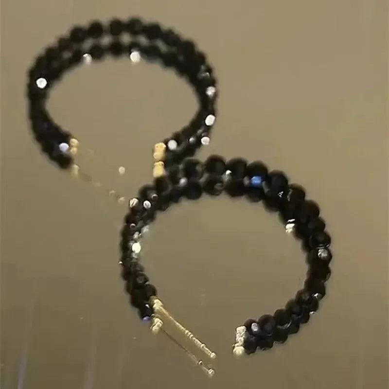Boucles d'oreilles créoles ouvertes composées de perles à facettes noires, monture dorée - Style chic et élégant.