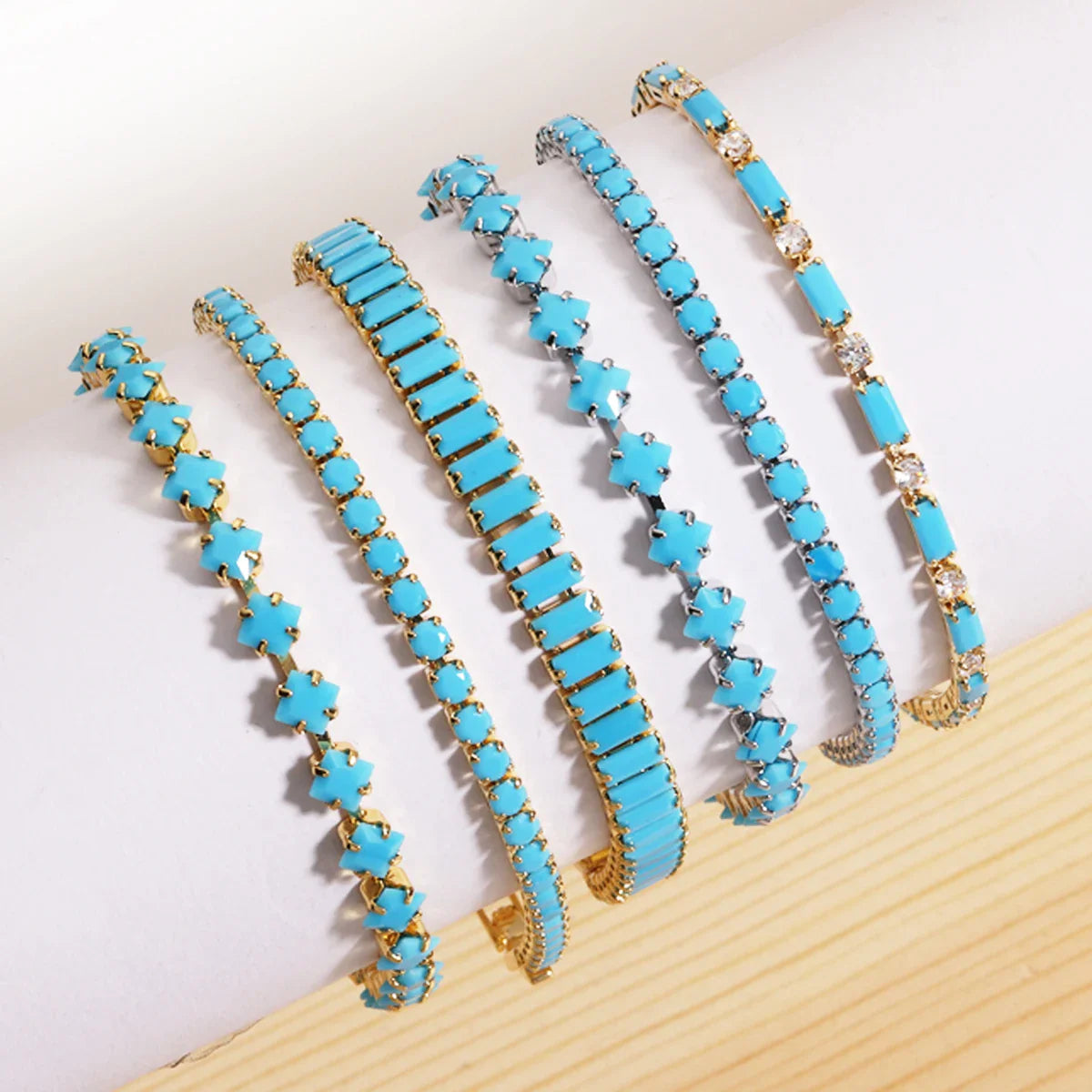 Assortiment de bracelets rivières dorés et argentés sertis de pierres turquoise synthétiques : formes carrées, étoiles et rectangulaires.